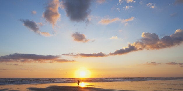 New Zealand, View of man carrying backpack walking along beach at sunset