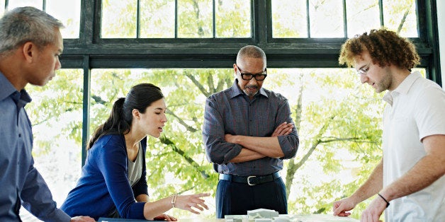 Four architects examining plans at table in office