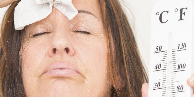 Portrait beautiful mature woman suffering from heat, high temperature, fever, with drops of sweat runing down face and thermometre in hand, isolated on white.