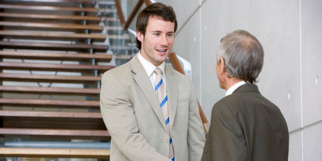 Low angle view of a younger and senior businessman shaking hands. The younger man is standing on a staircase. Vertical shot.