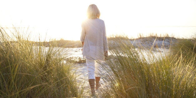 Senior woman, aged 64, walking on a beach at sunset