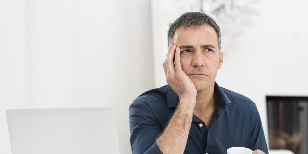 Portrait Of A Worried Mature Man With Laptop Holding Cup