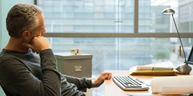 Man sitting at desk in office, looking away in thought