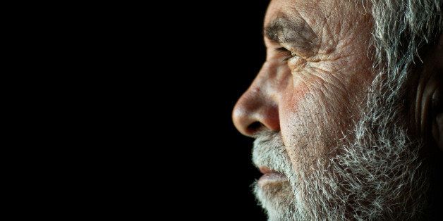 Low key side portrait of an old man with a white beard.