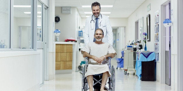 Happy doctor pushing disabled man in wheelchair at hospital corridor