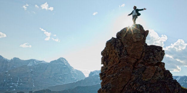 Man stands on peak, arms outstretched.