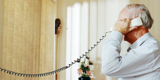 Senior man holding telephone receiver, side view