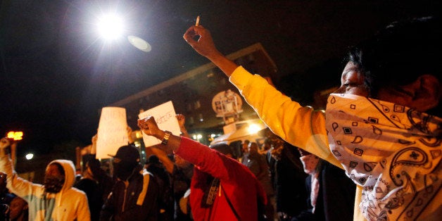 Protesters raise their hands as a circling police helicopter illuminates the area on the third night of curfew, Thursday, April 30, 2015, in Baltimore. (AP Photo/Alex Brandon)