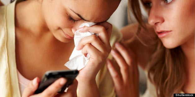 Closeup portrait of a young girl holding a mobile phone in sorrow with a friend consoling her