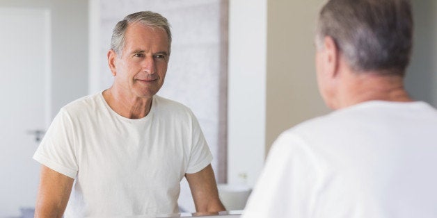 Mature man looking at his reflection in mirror in bathroom