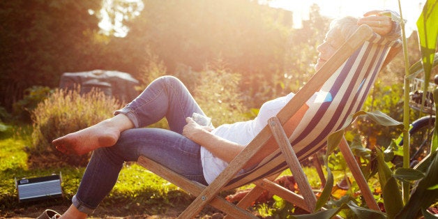 Senior woman drinking iced water while relaxing on a deckchair in an allotment during late afternoon