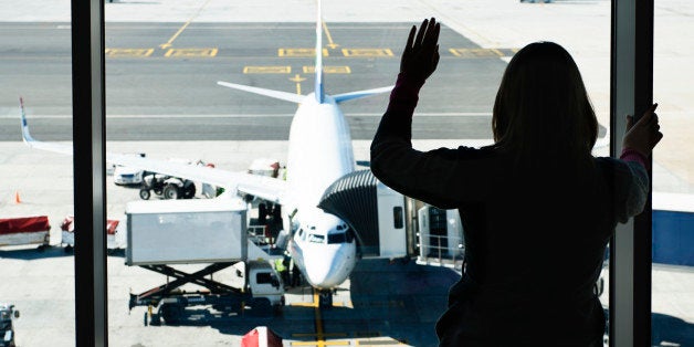 Silhouetted woman waves through airport window at plane