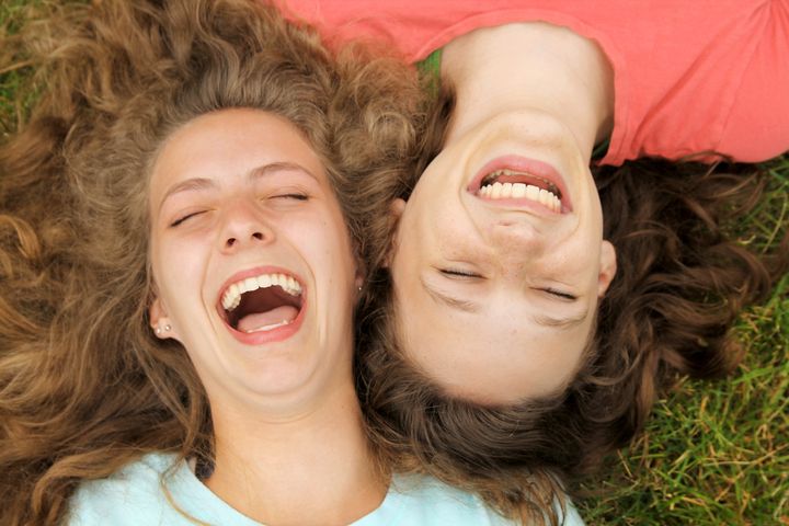 Happy teenagers friends lying on a grass laughing in a park