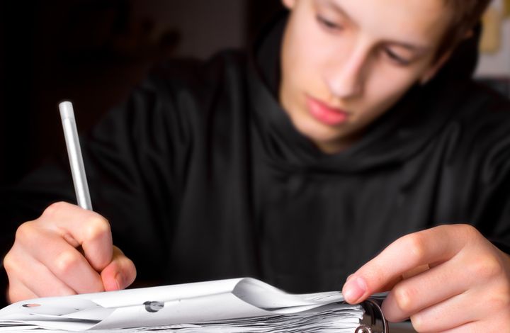 Closeup of teenage boy's hands and papers as he does school work