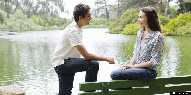 Two Teenagers on a Park Bench By The Water Smiling To Each Other