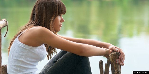 Pretty teenage girl sitting on the dock beside the river on beautiful summer day.