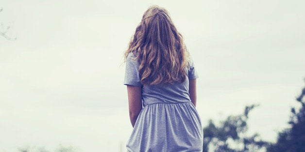 A blonde girl's back as she sits on a log and looks up to the sky