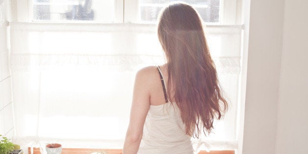 Young woman having breakfast in her kitchen, back view