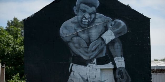 A woman photographs a mural of Muhammad Ali's 1965 victory over Sonny Liston June 10, 2016 in Louisville, Kentucky.A mass funeral procession for Muhammad Ali began Friday in his hometown Louisville, with a hearse carrying the boxing legend's remains heading into the streets where thousands gathered to say goodbye. / AFP / Brendan Smialowski (Photo credit should read BRENDAN SMIALOWSKI/AFP/Getty Images)