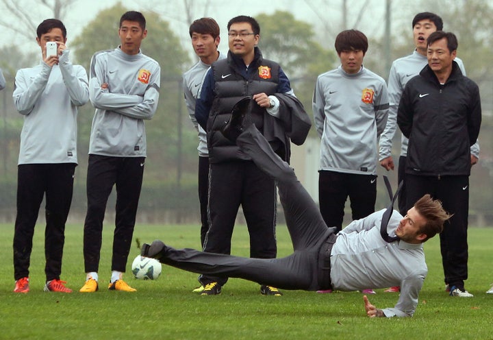 Football superstar David Beckham (R) falls down after illustrating how to take a free kick during a visit to the Zall Footbal