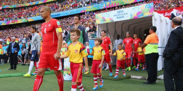 SALVADOR, BRAZIL - JUNE 20: Gokhan Inler of Switzerland leads his team to the field with their player escorts during the 2014 FIFA World Cup Brazil Group E match between Switzerland and France at Arena Fonte Nova on June 20, 2014 in Salvador, Brazil. (Photo by Elsa/Getty Images)