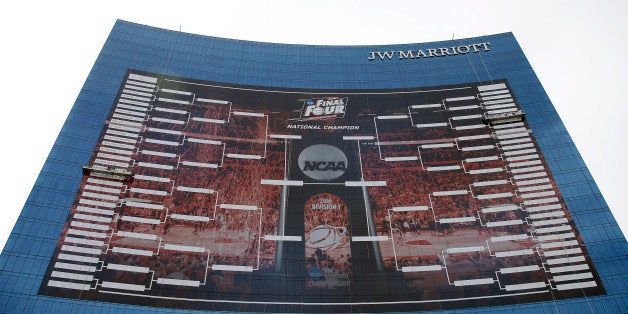 Workers add team names to a 2015 NCAA Division I Menâs Basketball Championship bracket that is displayed on the side of th