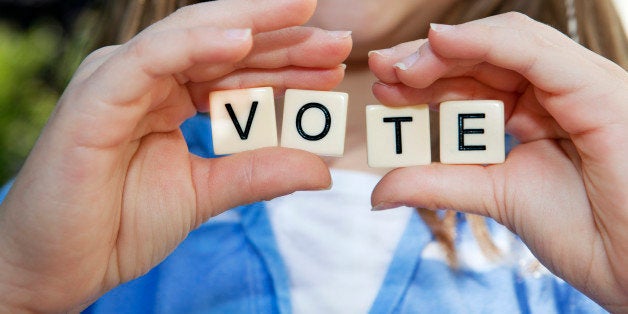 Young girl holding small block letters with message: Vote