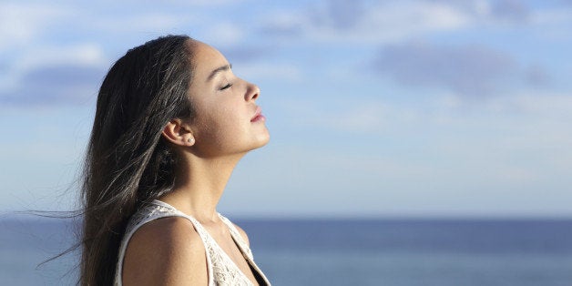 Profile of a beautiful arab woman breathing fresh air in the beach with a cloudy blue sky in the background