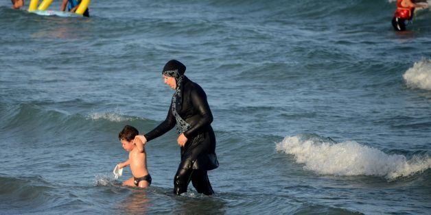 A Tunisian woman wearing a 'burkini', a full-body swimsuit designed for Muslim women, walks in the water with a child on August 16, 2016 at Ghar El Melh beach near Bizerte, north-east of the capital Tunis. / AFP / FETHI BELAID (Photo credit should read FETHI BELAID/AFP/Getty Images)