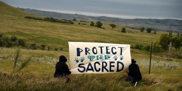 People hang a sign near a burial ground sacred site that was disturbed by bulldozers building the Dakota Access Pipeline (DAPL), near the encampment where hundreds of people have gathered to join the Standing Rock Sioux Tribe's protest of the oil pipeline that is slated to cross the Missouri River nearby, September 4, 2016 near Cannon Ball, North Dakota. Protestors were attacked by dogs and sprayed with an eye and respiratory irritant yesterday when they arrived at the site to protest after learning of the bulldozing work. / AFP / Robyn BECK (Photo credit should read ROBYN BECK/AFP/Getty Images)