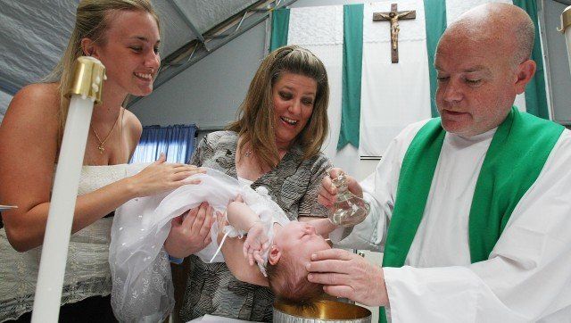 WAVELAND, MS - AUGUST 19: Priest Cuthbert O'Connell baptizes baby Trish Cucurullo as mother Sheena Cucurullo (L) and godmother Shannon Ball assist following Sunday Mass at Saint Clare Catholic Church's temporary tent sanctuary August 19, 2007 in Waveland, Mississippi. The church, whose building was destroyed by Hurricane Katrina in 2005, has yet to be rebuilt because they are still awaiting federal regulatory approval before beginning construction. The second anniversary of Hurricane Katrina is August 29. (Photo by Mario Tama/Getty Images)