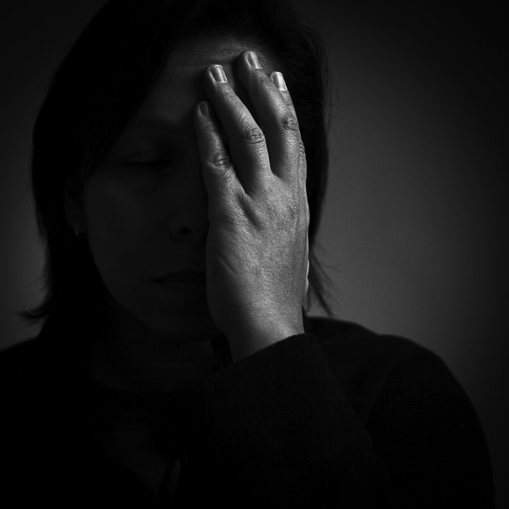 Dark female portrait with hand covering half of face.