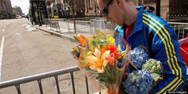 A man in a Boston Marathon 2013 shirt carries flowers near a memorial site at Boylston and Arlington streets along the course of the Boston Marathon on April 16, 2013, a few blocks from where two explosions struck near the finish line of the Boston Marathon on April 15. The explosives used in the Boston Marathon bombings were likely homemade devices full of nails and metal fragments designed to cause widespread injury, according to initial reports. A day after an attack that left three dead and more than 170 wounded, the FBI and Boston police declined to reveal details of their probe, or whether they suspected the assault was linked to foreign or domestic extremists. AFP PHOTO/Don Emmert (Photo credit should read DON EMMERT/AFP/Getty Images)