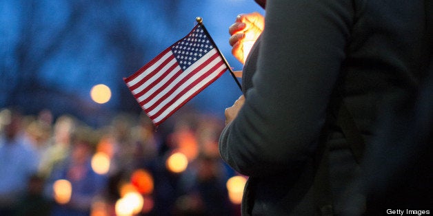 A mourner holds a candle and a U.S. flag during a vigil for Martin Richard, one of three killed in the Boston Marathon bombings, at Garvey Park in Boston, Massachusetts, U.S., on Tuesday, April 16, 2013. Richard, an 8-year-old from Boston's Dorchster neighborhood, was among the dead in blasts that also injured his mother and sister. Photographer: Scott Eisen/Bloomberg via Getty Images