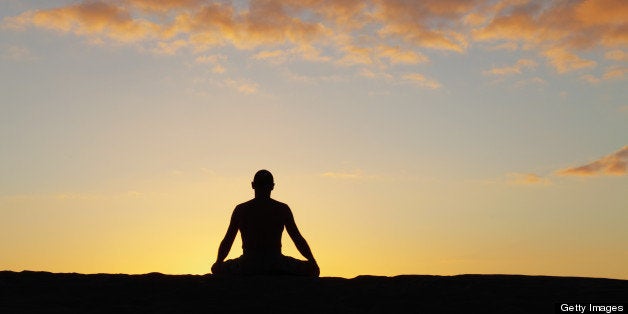 silhouette of a meditating man against sunset sky