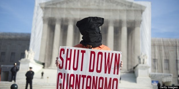 A protestor wears an orange prison jump suit and black hood on their head during protests against holding detainees at the mi