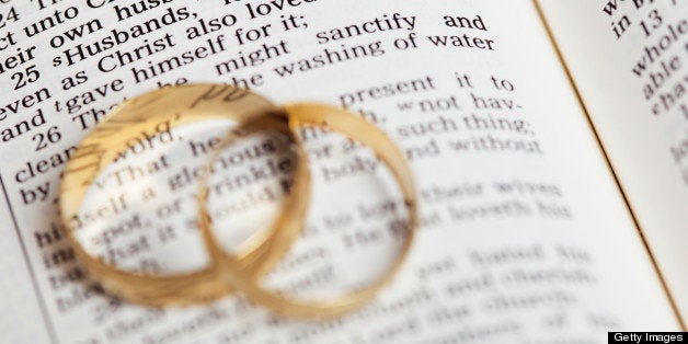 Gold wedding bands placed on a King James Version Bible. The passage is Ephesians 5