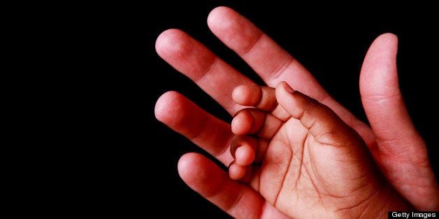 The hand of an African child resting in the palm of her father's hand. Shot against a black background.