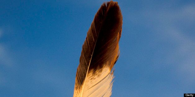Native American hand holding a sacred eagle feather high up against a blue sky background