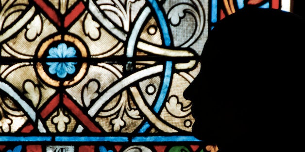 The silhouette of a man in prayer, with the backdrop of stained glass design, to signify the location being in church. This image was taken in the interior of Notre Dame of Paris, France.