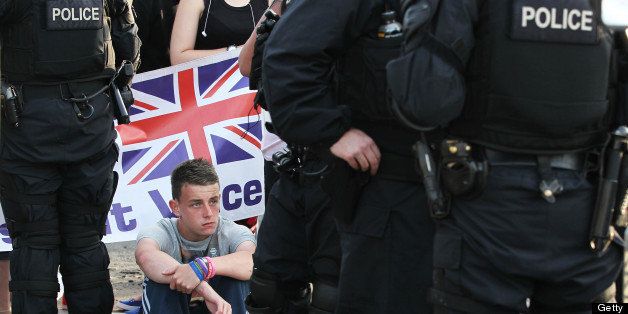 A young loyalists protester sits down on the ground next to riot police in North Belfast, Northern Ireland on July 13, 2013. Trouble flared after police tried to enforce a decision by an adjudication body banning the Orange Order from marching through a Catholic republican area of Belfast during their annual July 12 march, which commemorates King William of Orange's victory over Catholic King James II in 1690. Hundreds of extra police were deployed to Northern Ireland on July 13 following a night of rioting in Belfast that left 32 officers injured and a politician hospitalised. AFP PHOTO / PETER MUHLY (Photo credit should read PETER MUHLY/AFP/Getty Images)