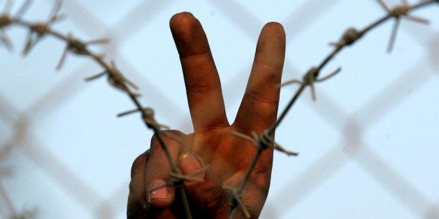 RAFAH, GAZA - JANUARY 24: A Palestinian man stand next to the fence as he flashes V-sign while people (not pictured) transport goods they bought in Egypt back into the Gaza Strip, after they crossed the Rafah border into Egypt over a barrier destroyed by masked Palestinian militants overnight January 24, 2008 in Rafah, Gaza . Thousands of Palestinians poured through dozens of holes in the wall, rushing to buy food and other staples that are in short supply due to an Israeli blockade of Hamas-controlled Gaza. (Photo by Abid Katib/Getty Images)