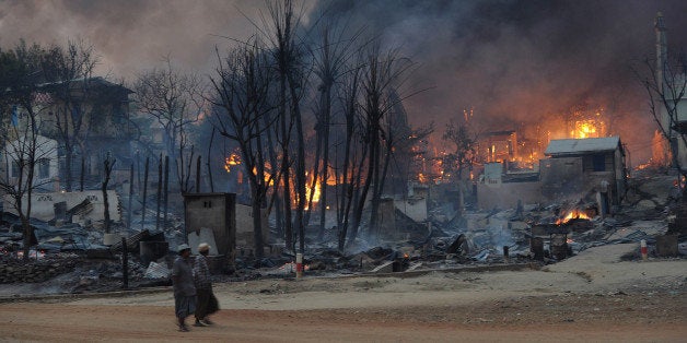 Residents walk past buildings burning in riot-hit Meiktila, central Myanmar on March 21, 2013. At least 10 people have been