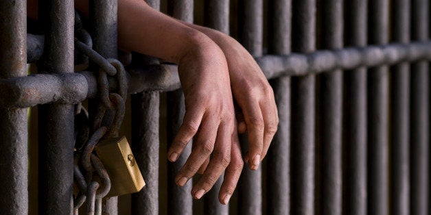 Close up of hands, behind the bars of a prison.