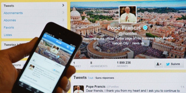 A man holds a smartphone showing Pope Francis' first tweet in front of a computer screen showing the same tweet on March 17,