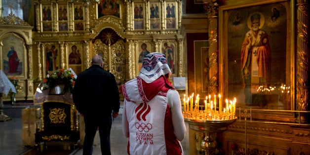 A Russian woman wearing a jacket of the Russian Olympic team prays inside St. Michael the Archangel Cathedral, Tuesday, Feb.
