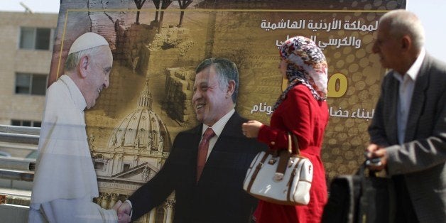 A Jordanian Muslim woman walks past a poster in Amman on May 22, 2014 showing Jordan's King Abdullah II (C) shaking hands with Pope Francis during his visit to the Vatican. Jordan expressed hope that Pope Francis's visit to the Holy Land would help the cause of regional stability, including the advancement of the stalled Middle East peace talks. AFP PHOTO / PATRICK BAZ (Photo credit should read PATRICK BAZ/AFP/Getty Images)