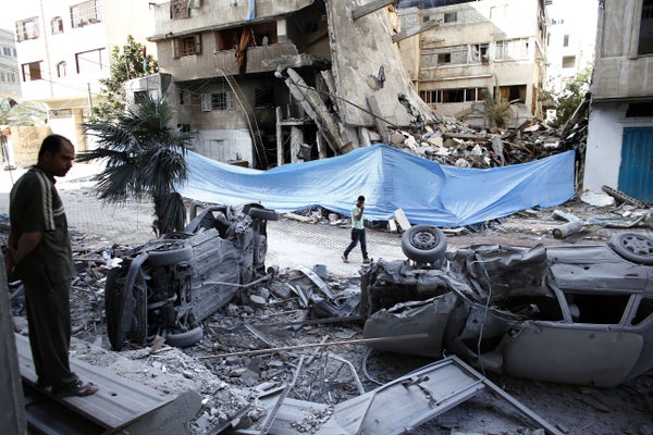 Palestinians look at damaged cars amid the rubble of destroyed buildings following an Israeli air strike on July 14, 2014 in 