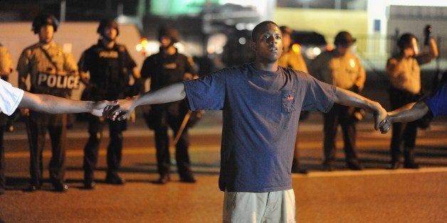 A protester joins hands with community leaders to form a barrier between police officers and protesters in attempt to diffuse the escalation between the two, during a peaceful protest in Ferguson, Missouri early on August 20, 2014. Police lowered their profile on August 19, and refrained from using tear gas, to allow a more orderly night of protests in this St Louis suburb 10 days after the police shooting of an unarmed black teenager. AFP PHOTO / Michael B. Thomas (Photo credit should read Michael B. Thomas/AFP/Getty Images)