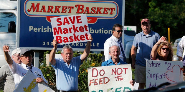 Protesters hold signs and taunt a car entering the site of a Market Basket Supermarket job fair in Andover, Mass., Wednesday,